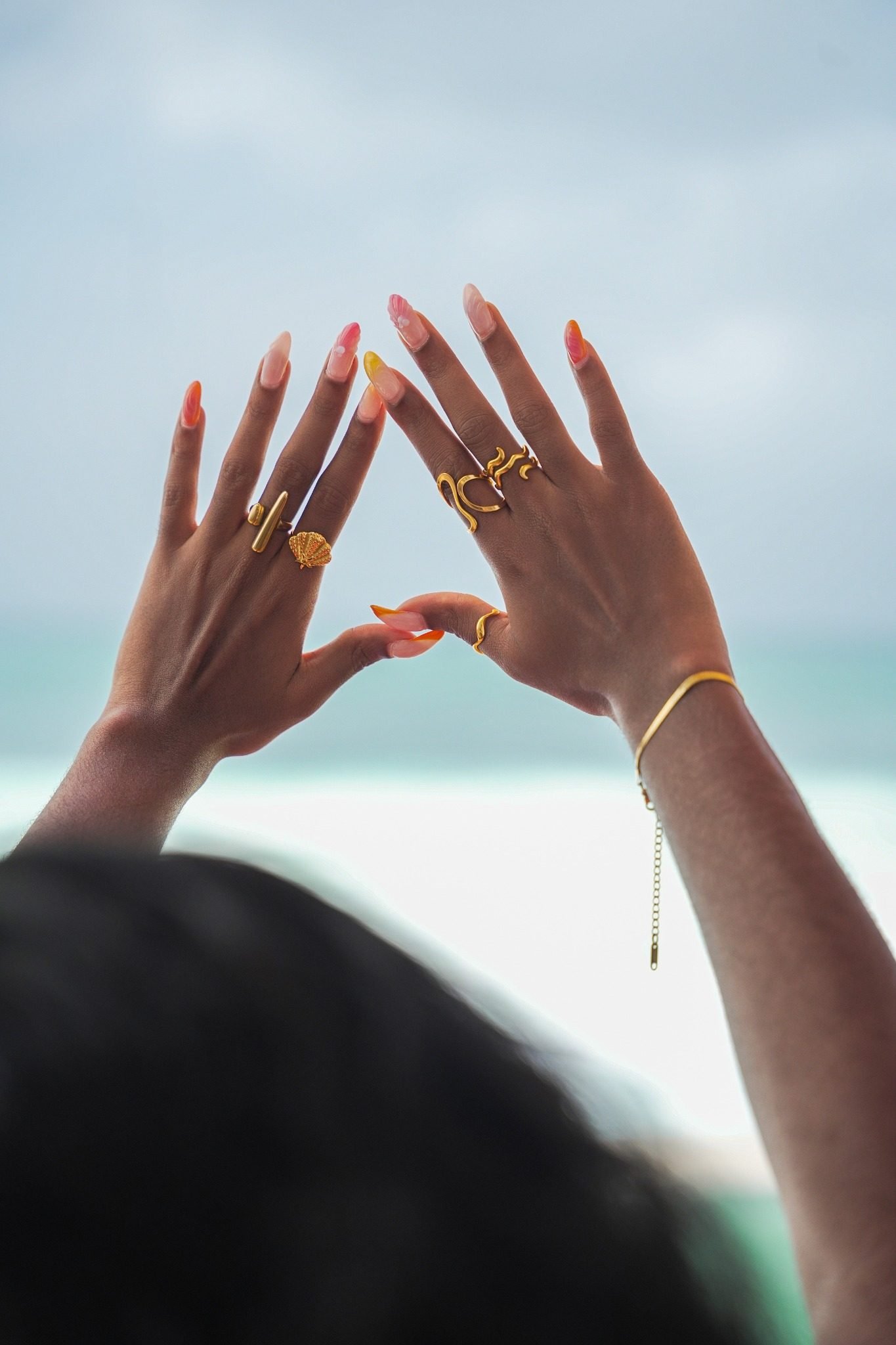 Mains levées vers le ciel, bagues et bracelet dorés